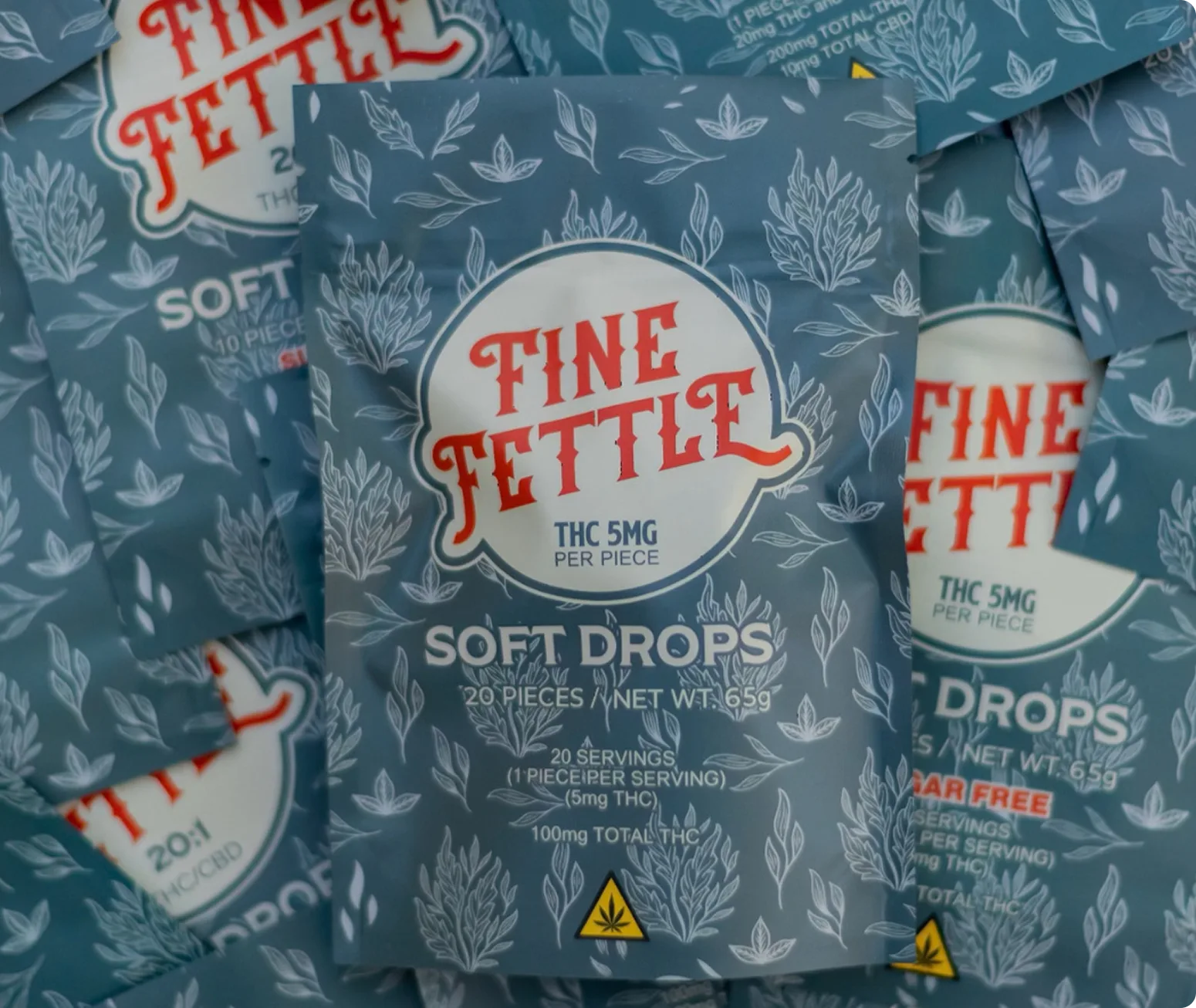 A close-up of Fine Fettle Soft Drops packaging showing “THC 5mg per piece” and “20 pieces” on a blue background with white botanical illustrations.